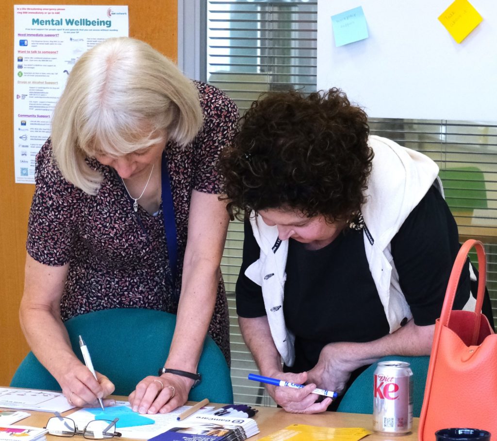 Two women having a conversation about menopause and writing positit notes to add to a poster